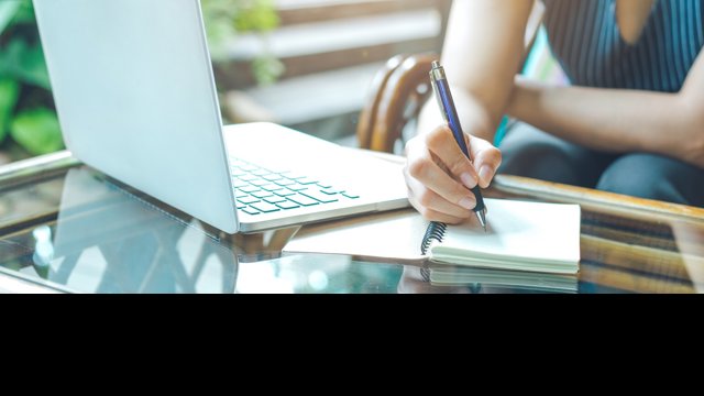 Archivo - Mujer escribiendo a mano con papel y bolígrafo junto a un ordenador portátil.