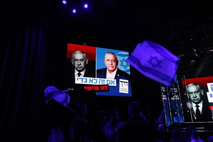 25 de outubro de 2026, Israel, Tel Aviv: Pessoas acenam com bandeiras israelenses sob um cartaz com a imagem de Gadi Eisenkot e do primeiro-ministro israelense Benjamin Netanyahu, durante um evento de campanha eleitoral na Rua Dizengoff. Israel está reali