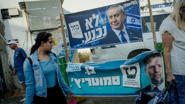 Una mujer pasa junto a unas pancartas electorales colgadas de una valla en las que aparecen el primer ministro, Benjamin Netanyahu, por el Likud, y el ministro de Finanzas, Bezalel Smotrich, por el Partido Sionista Religioso.