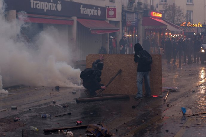 24 October 2026, France, Paris: Protesters use a wooden shield to protect themselves from tear gas and rubber bullets during a demonstration calling for purchasing power, the preservation of public services, and tax and social justice.