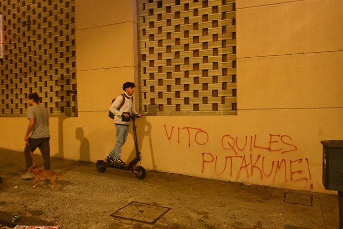 Una persona pasa en patinete por una pintada sobre VIto Quiles, tras una concentración de diversos agentes sociales con el lema  "Euskal Herrian Faxismoaren Ez!", en Bilbao