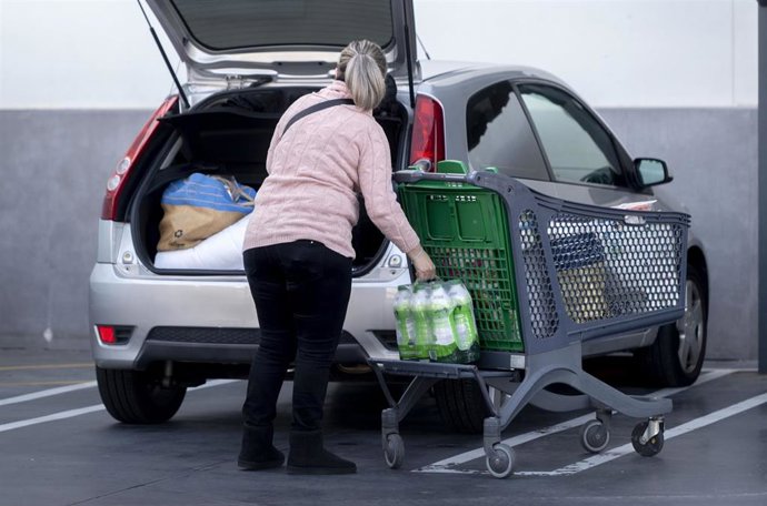 Archivo - Una mujer mete la compra en el maletero de su vehículo tras salir de un supermercado