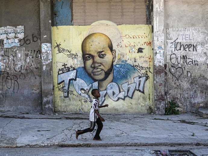 Archivo - Arquivo - 21 de fevereiro de 2026, Porto Príncipe, Haiti: Um menino passa por um mural pintado em memória de George Floyd na parede do Colégio Saint Louis de Bourdon, na capital Porto Príncipe. Apesar do perigo, as famílias vivem no território c