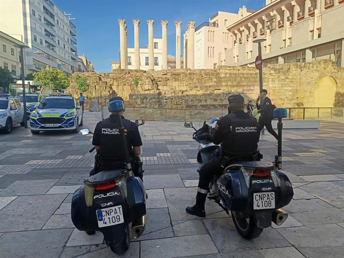 Dos agentes de la Policía Nacional en motocicleta, integrados en un dispositivo preventivo en la calle Capitulares, ante el Templo Romano y el  Ayuntamiento de Córdoba.